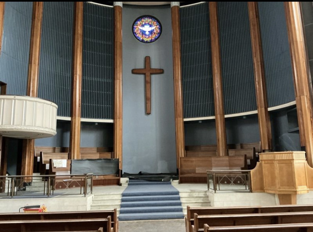 Interior of City Temple with timber columns, a wooden cross, a circular stained-glass window and pews