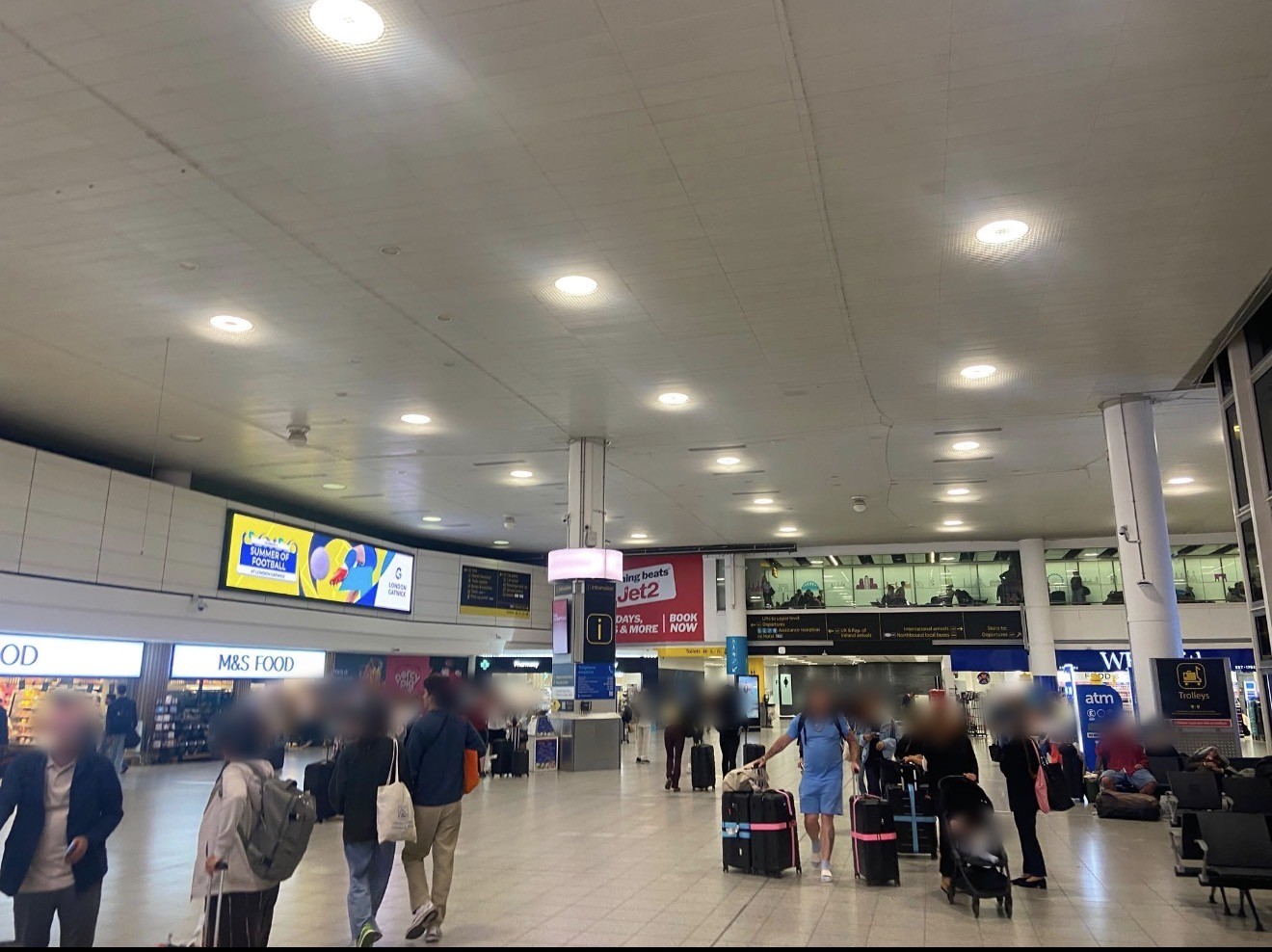 Passengers with luggage walking through a busy concourse in Gatwick Airport South Terminal