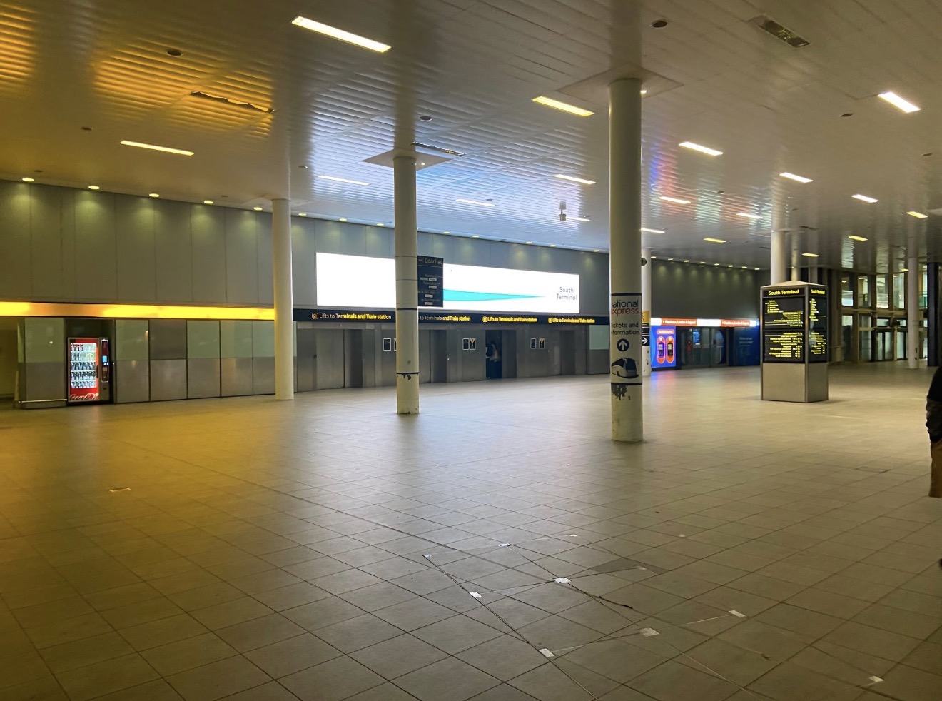 Quiet lower-level concourse at Gatwick Airport South Terminal with columns, lifts and a departures board